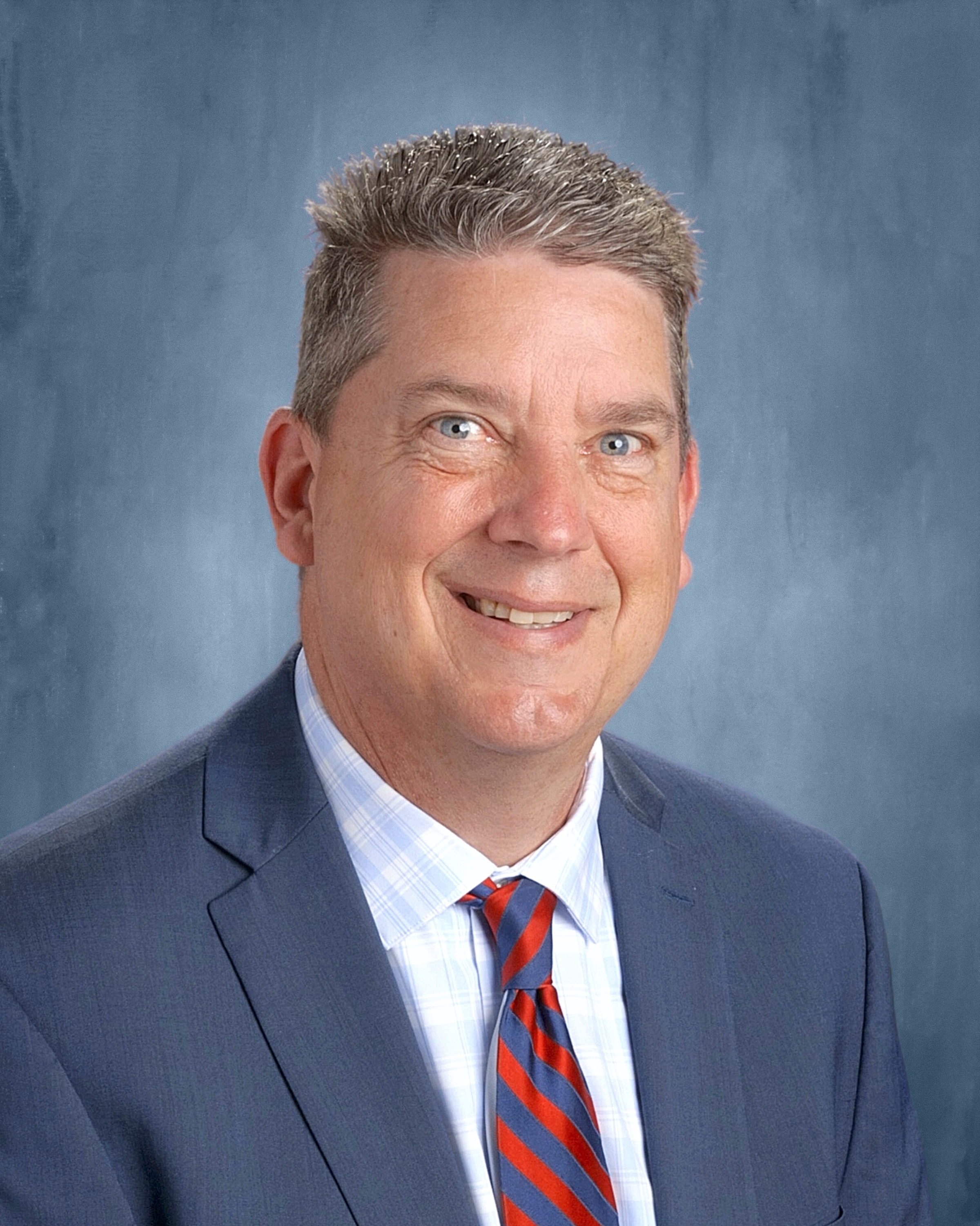 A man in a light blue suit smiles at the camera